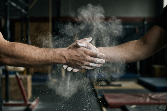 Chalk dust bursting from a lifter's chalked hands in a gym
