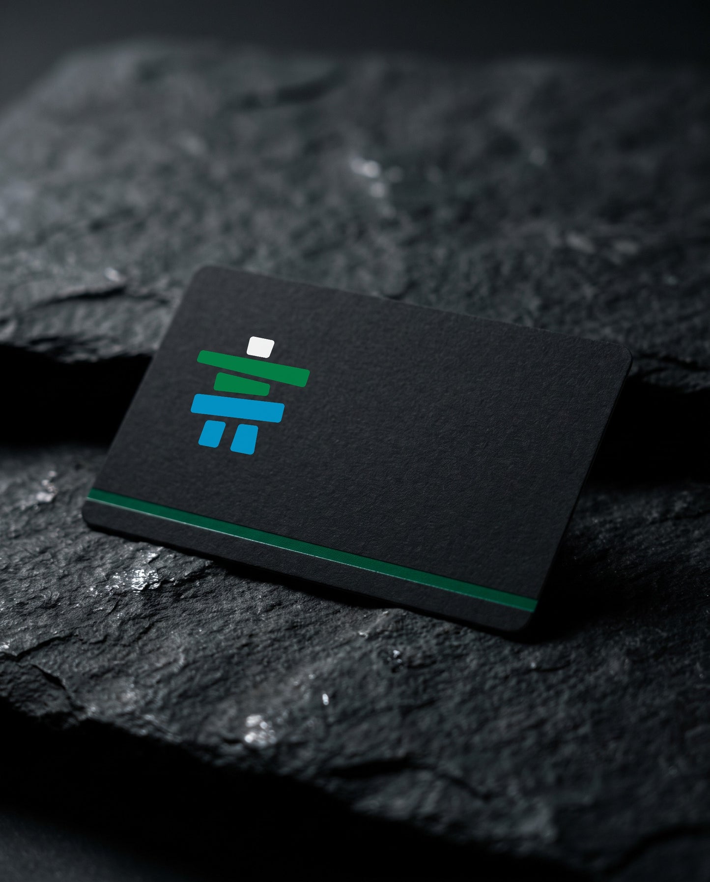 Matte black Inclusive Fitness gift card with the inukshuk logomark, resting on dark slate