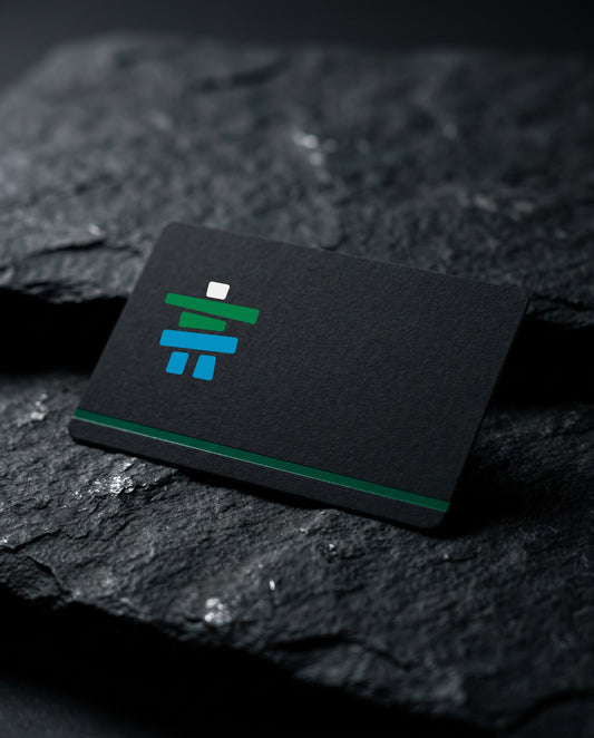 Matte black Inclusive Fitness gift card with the inukshuk logomark, resting on dark slate